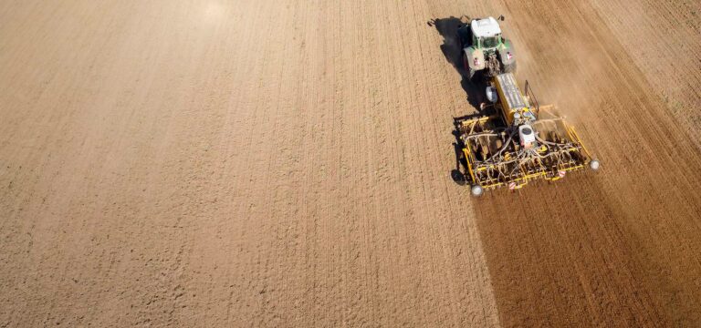 Ein Traktor mit Erdzugmaschine fährt auf einem Feld aus Erde.
