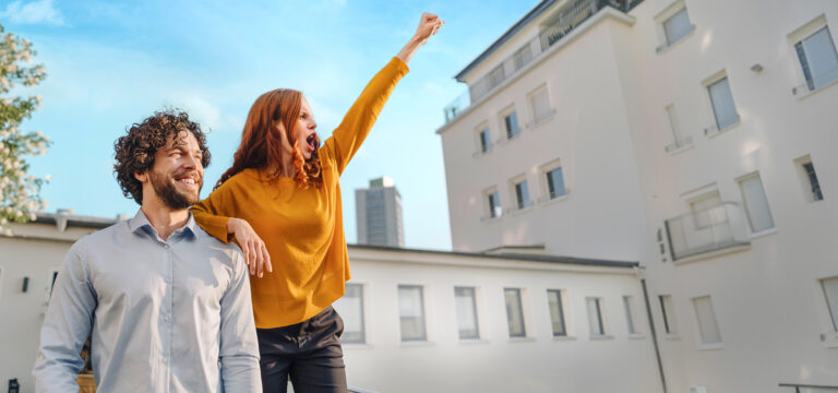 Ein Mann und eine Frau stehen mit erhobenen Armen auf einem Dach.