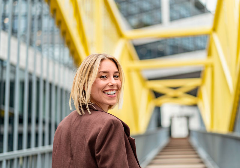 Eine fröhliche junge Frau auf einer Brücke mit gelbem Geländer.