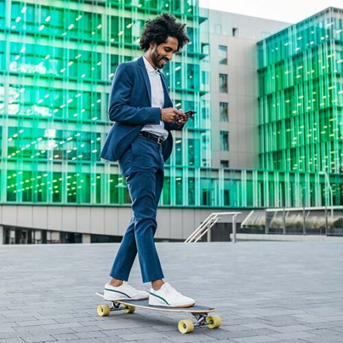 Ein Geschäftsmann rollt auf einem Skateboard durch die Stadt und schaut auf sein Smartphone.