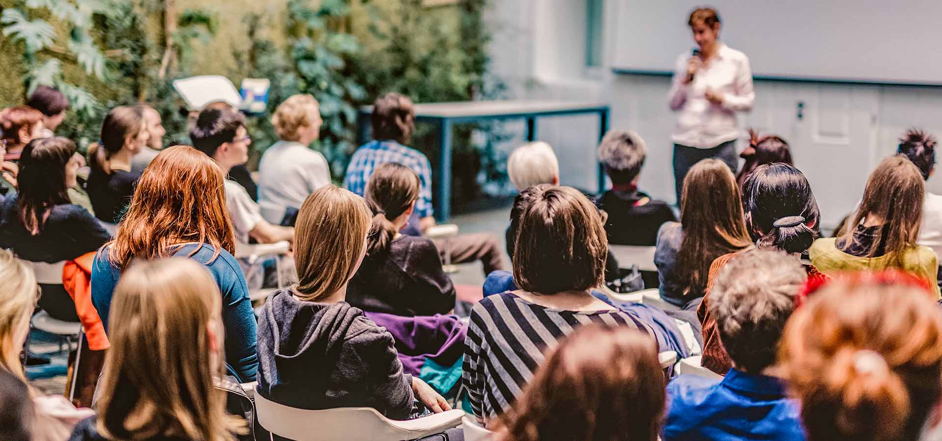 Eine Gruppe junger Menschen sitzt in einem Vorlesungssaal und hört einer Dozierenden zu