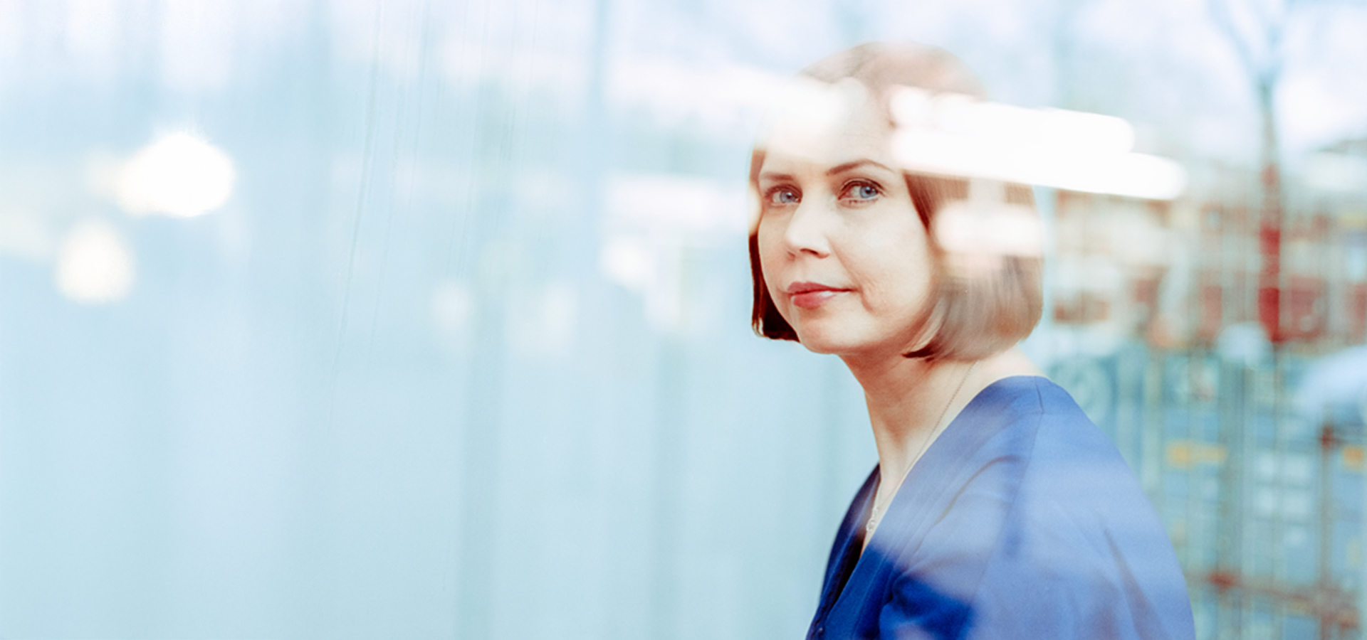 Katja Krüger schaut durch Glasfläche, reflektierte Umgebung im Hintergrund